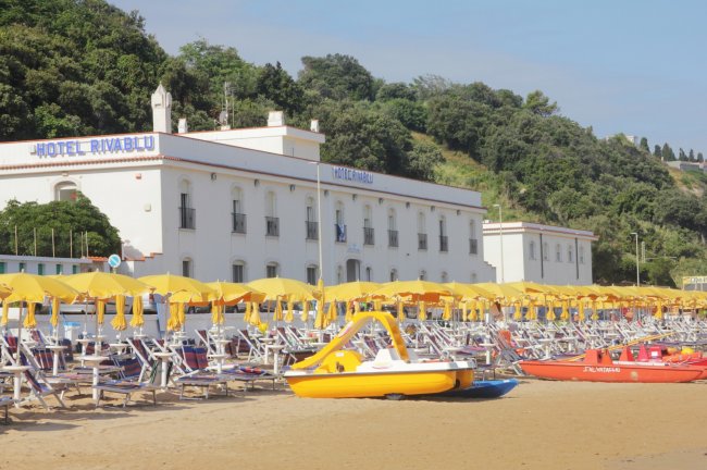 Spiaggia con ombrelloni gialli e hotel sullo sfondo.