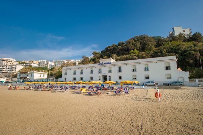 Una spiaggia con ombrelloni gialli e un hotel bianco sullo sfondo.