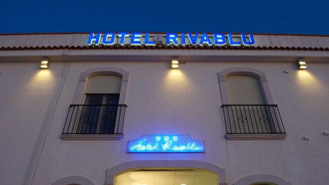Facciata dell'Hotel Rivablu, con insegne blu illuminate di notte.
