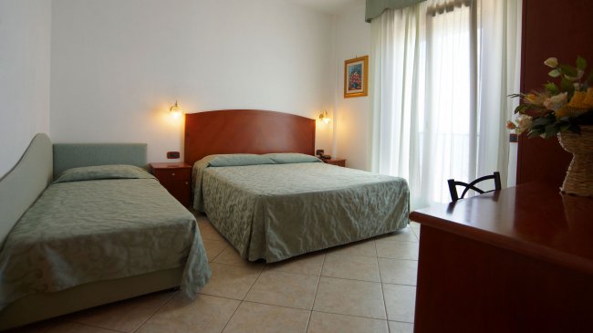 Stanza con letto matrimoniale e singolo, arredamento semplice e porte finestre.