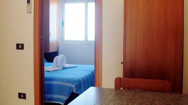 Stanza da letto con letto blu e asciugamani a forma di cigni. Vista dalla porta.