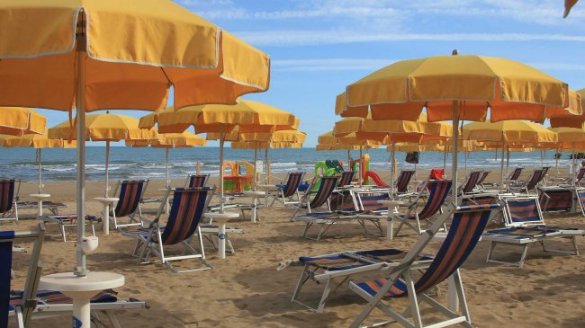 Spiaggia con ombrelloni gialli e lettini blu a righe sotto un cielo sereno.