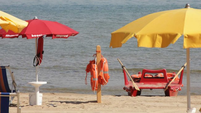Spiaggia con ombrelloni gialli e rossi, una sedia a sdraio rossa e salvagenti.
