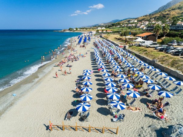 Spiaggia con lettini e ombrelloni blu e bianchi, persone che si godono il sole.