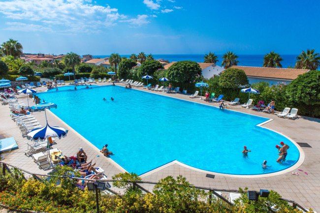 Piscina azzurra con lettini e ombrelloni in un resort, cielo sereno sullo sfondo.
