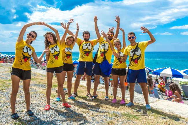 Gruppo di persone in magliette gialle allegre posa davanti al mare.