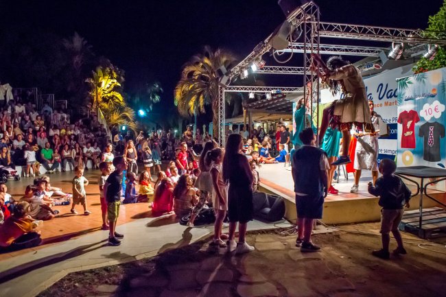 Spettacolo notturno all'aperto con pubblico seduto e in piedi davanti a un palco.