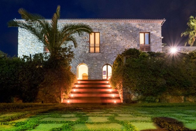 Edificio in pietra con scale illuminate e vegetazione.