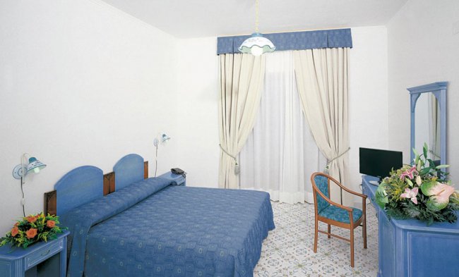 Camera da letto con arredi blu e pareti bianche, tende chiuse.