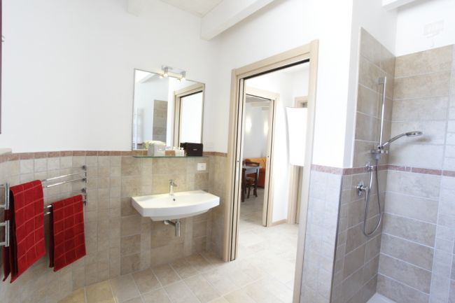 Bagno moderno con doccia a pioggia, specchio e portasciugamani con asciugamani rossi.
