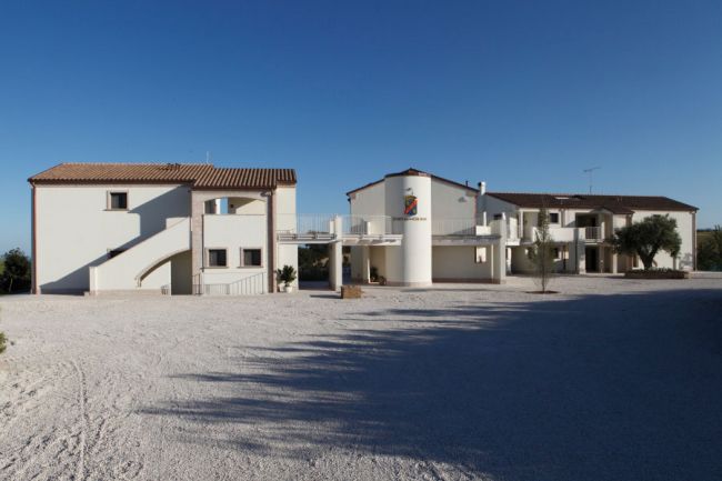 Un edificio modernista bianco su un ampio cortile di ghiaia, con cielo azzurro sopra.