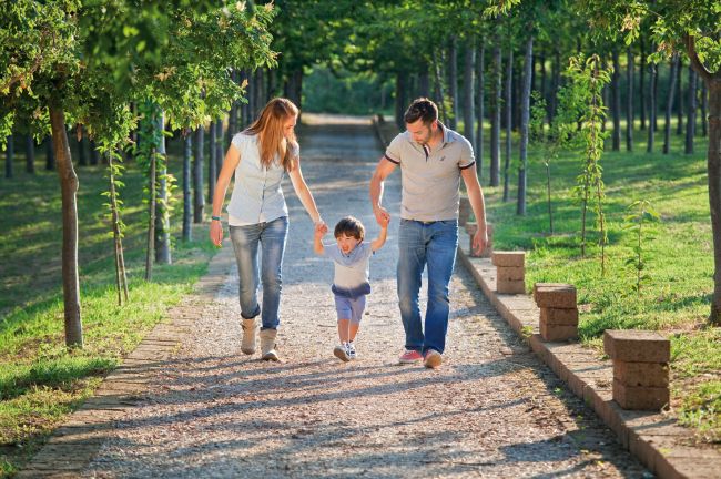 Due adulti e un bambino camminano felici in un viale alberato, tenendosi per mano.