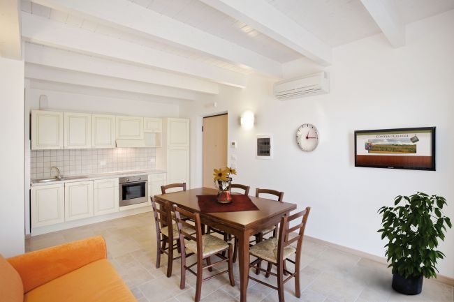 Cucina e sala da pranzo luminosa con tavolo in legno, sedie, cucina bianca e pianta.