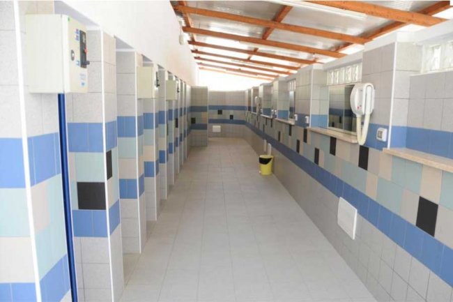 Corridoio di bagni pubblici con piastrelle a motivi blu e grigi e soffitto con travi in legno.