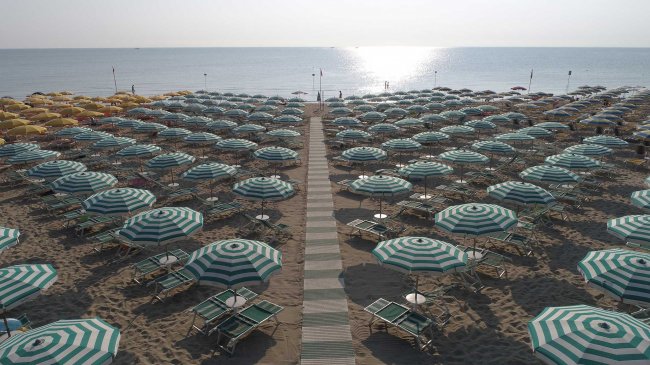 Spiaggia affollata con ombrelloni a righe verde e bianco, con passerella centrale verso il mare.