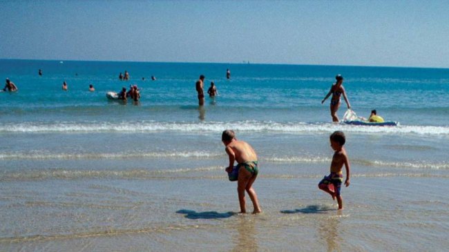 Bambini giocano al mare mentre adulti nuotano nelle vicinanze.