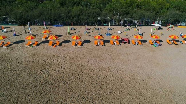 Spiaggia sabbiosa con ombrelloni e sdraio arancioni.