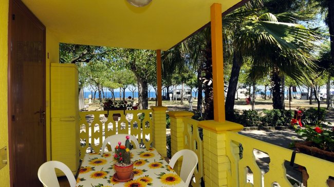 Tavolo con tovaglia a fiori su veranda gialla, vista mare e alberi.