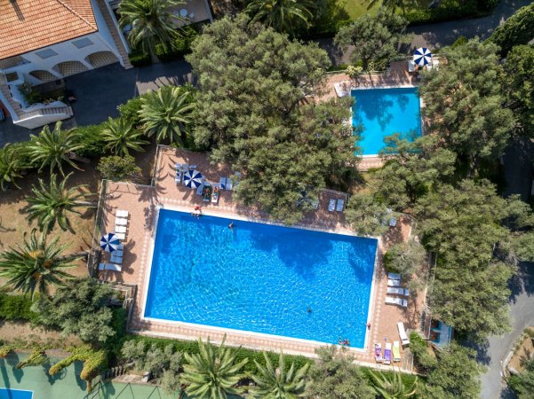 Vista dall'alto di due piscine circondate da alberi e ombrelloni a righe.