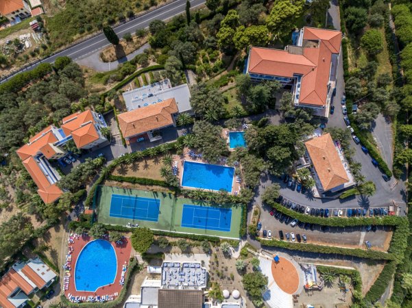 Vista aerea di un complesso con piscine e campi da tennis circondati da vegetazione.