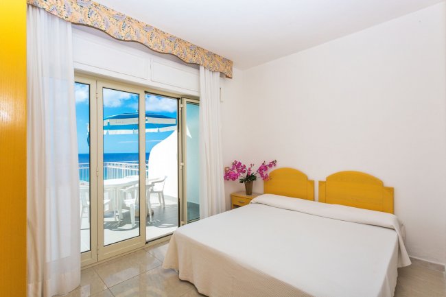 Una camera con letto matrimoniale, fiori sul comodino e vista mare.