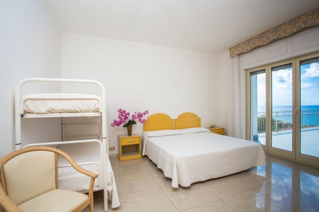 Camera con vista mare, letto matrimoniale, letto a castello, e arredo giallo.