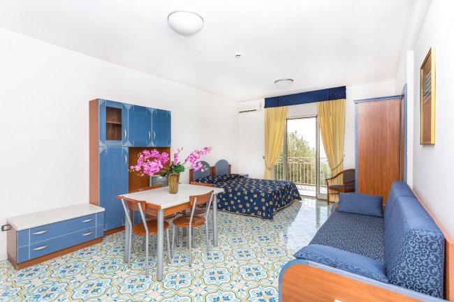 Monolocale con letto, divano blu, tavolo, e balcone.