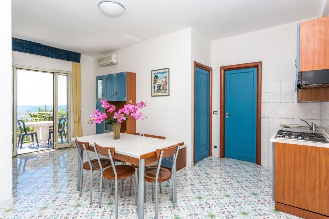 Sala da pranzo con tavolo, cucina e vista mare.