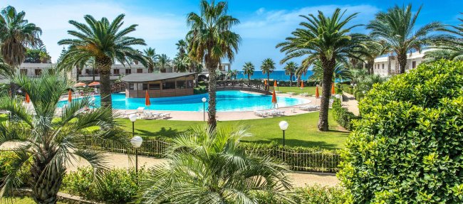 Piscina circondata da palme, con vista sul mare e lettini.