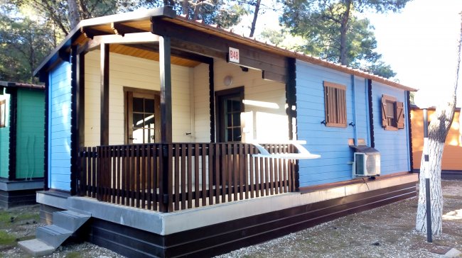 Una casetta in legno blu con veranda, situata in una zona alberata.