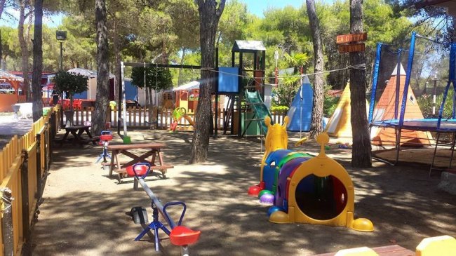 Parco giochi con altalene, scivoli e strutture colorate tra gli alberi.