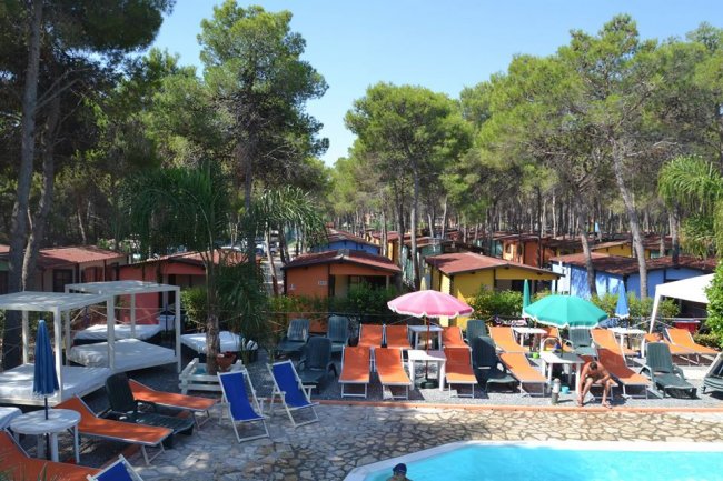 Piscina circondata da sdraio colorate e ombrelloni tra bungalow immersi nel verde.