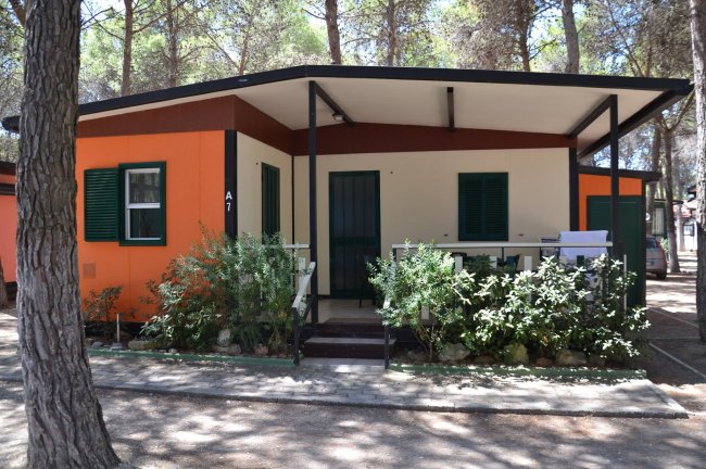 Casetta arancione e beige con veranda e piante davanti.