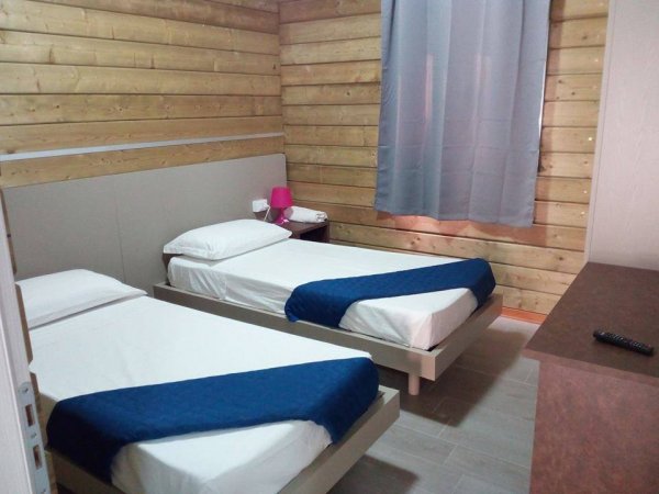 Due letti singoli con coperte blu, pareti in legno.