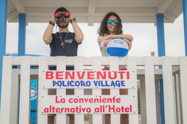Due persone dietro un'insegna di benvenuto a Policoro Village.