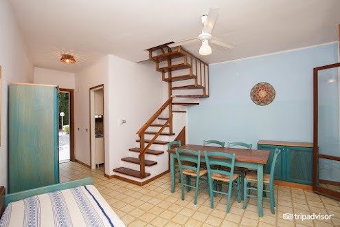 Soggiorno con tavolo, sedie, scala e ventaglio a soffitto.