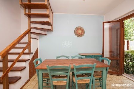 Sala da pranzo con scala in legno e tavolo con sedie verdi.