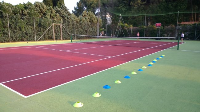 Campo da tennis rosso e verde con coni colorati lungo il bordo.