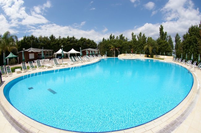 Grande piscina azzurra circondata da sedie a sdraio e alberi.