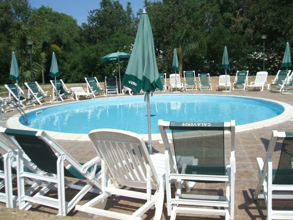 Piscina circolare con lettini e ombrelloni verdi.