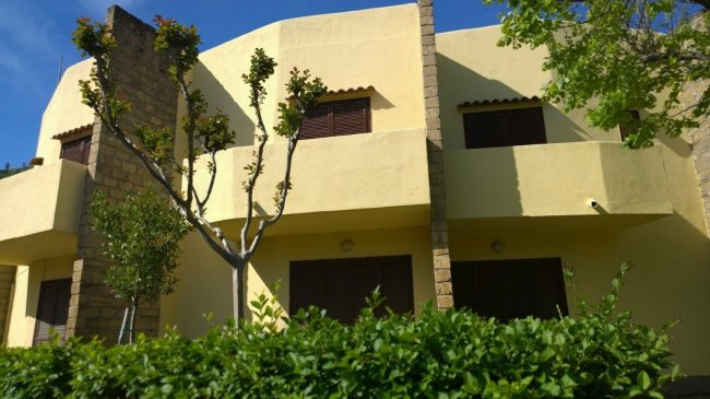 Edificio giallo con finestre scure e alberi circostanti.