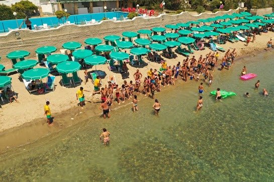 Spiaggia affollata con ombrelloni verdi.
