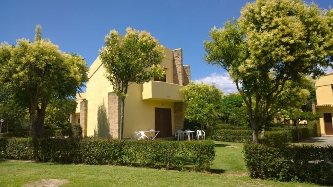 Un edificio giallo con giardino e alberi, mobili da esterno nel prato.