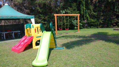 Un parco con uno scivolo colorato, altalene e un gazebo su prato.