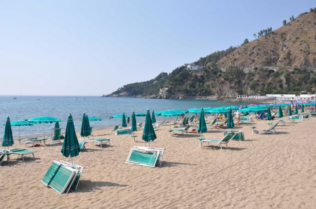 Spiaggia sabbiosa con lettini e ombrelloni verdi, mare calmo sullo sfondo.