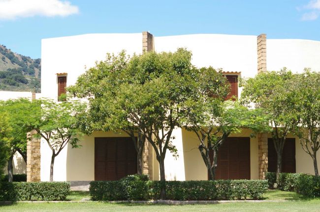 Struttura abitativa beige con porte scure, circondata da alberi e un prato ben curato.