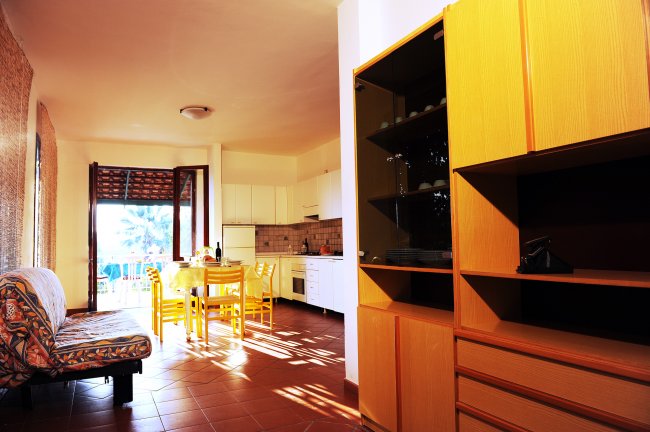 Cucina luminosa con tavolo giallo, sedie, divano a fantasia e credenza in legno.