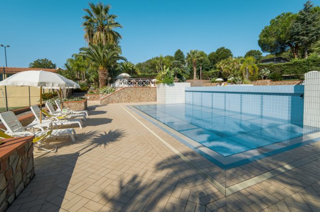 Una piscina con lettini bianchi e ombrelloni, circondata da palme.