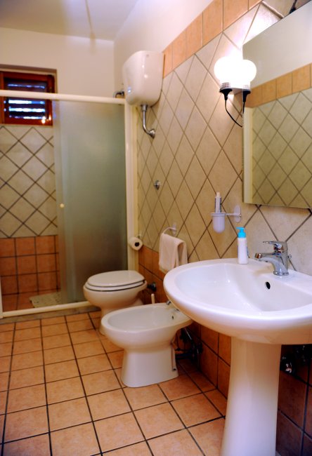 Un bagno con doccia, lavandino, bidet e WC. Rivestimento in piastrelle beige.