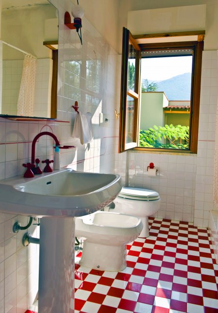 Un bagno con finestra, lavandino, bidet e WC. Piastrelle a scacchi rosse e bianche.